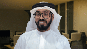 Emirati man wearing a traditional white kandura and black agal, smiling in an office setting.